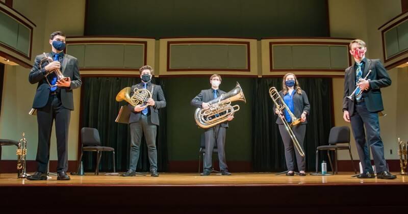 five students standing on a stage holidng brass instruments